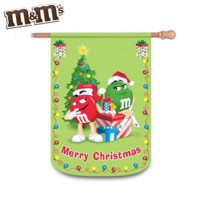 Get in the holiday spirit with this first-of-its-kind indoor/outdoor M&M'S&reg; decorative Christmas flag starring the charming "Red" and "Green" characters, available exclusively from The Hamilton Collection. This durable, waterproof decorative flag will be a delightful addition to your home, and a great way to celebrate the Christmas season!Showcasing cheerful "Red" and "Green" M&M'S characters exchanging gifts by a Christmas tree decorated with M&M'S candies, this festive Merry Christmas flag is machine washable and fade resistant, so the vivid colors and illustration will remain bright for years. The fitting message, "Merry Christmas" and holiday-themed border complete the M&M'S flag. What a great way to decorate your home for Christmas. Strong demand is expected. Order now!
