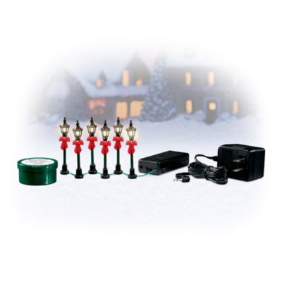What could be more magical than your Christmas Village bathed in the warm glow of classic lamplights, each decorated with a jaunty red bow! This handcrafted, six-piece lamppost set (batteries not included) features meticulously sculpted detail and comes with an AC/DC adapter.Adding this festive village lighting accessory set to your village display couldn't be easier! Just apply the DecorGreat artist's adhesive (included) with your finger or small tool to the bottom of each lamppost to keep it upright and stable. This adhesive adheres to virtually any non-porous surface and wipes right off! Give your Hawthorne Christmas Village a charming holiday glow at an attractive price. Order now!